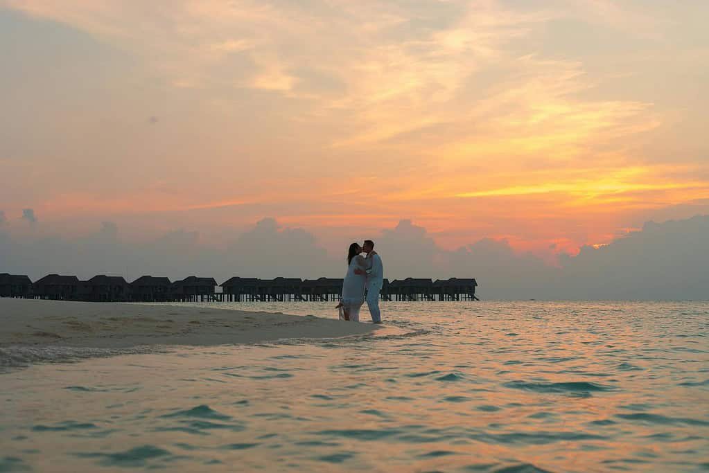 Couple Standing on White Sand Near Body of Water during Sunset