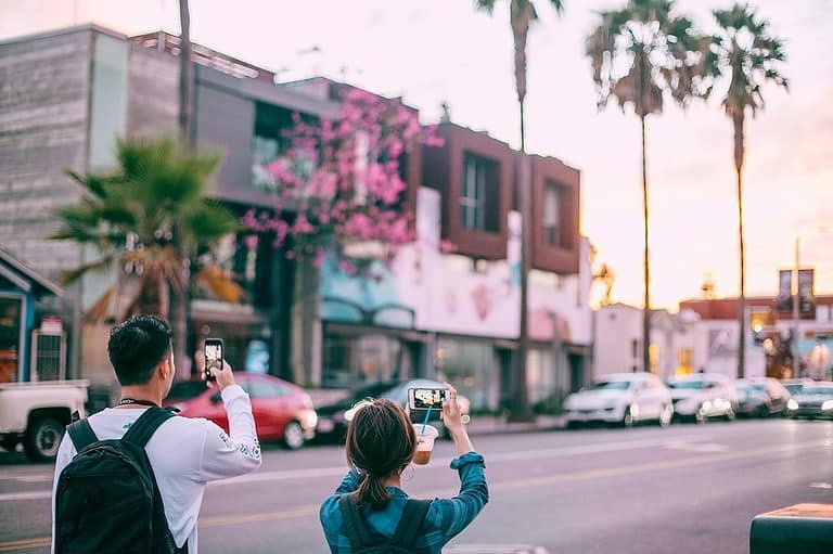 Unrecognizable tourists taking pictures on smartphone of tropical city street